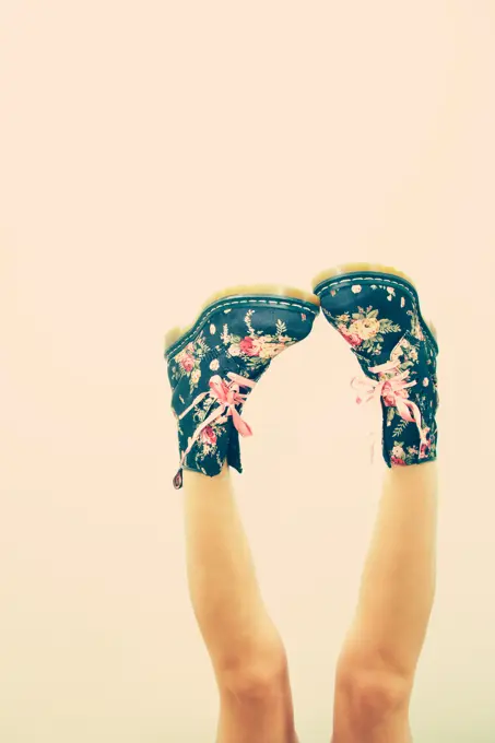 Unrecognizable woman with naked legs in blue boots with flowers and pink laces in studio on pink background;Faceless female with naked legs in boots in studio