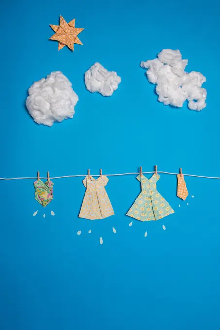 Cute paper dresses attached to rope against blue sky with clouds