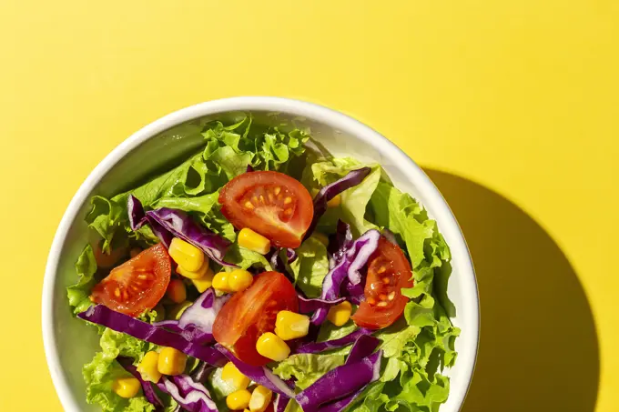 Fresh lettuce salad with Cherries tomatoes, red onion and corn, sunlight on pink background from above. Healthy food. Vegan food.