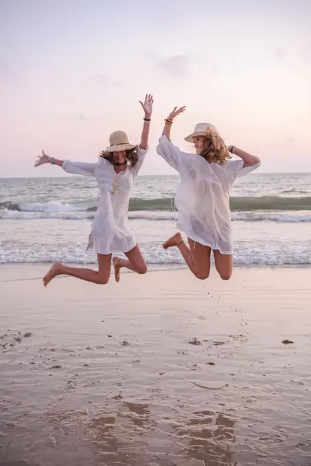 Smiling girlfriends in summer clothes barefoot in water on beach