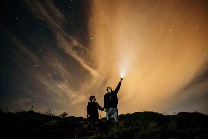 Carefree dad and son holding hands and observing starry sky while looking up and lighting with torch at night