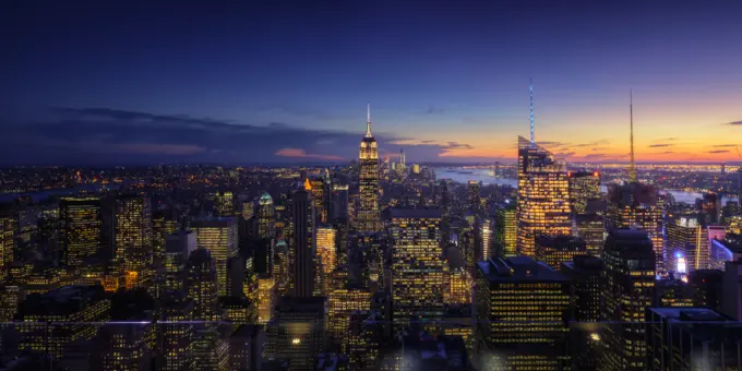 Wide angle drone view of illuminated skyscrapers located in downtown of modern city against cloudy sundown sky