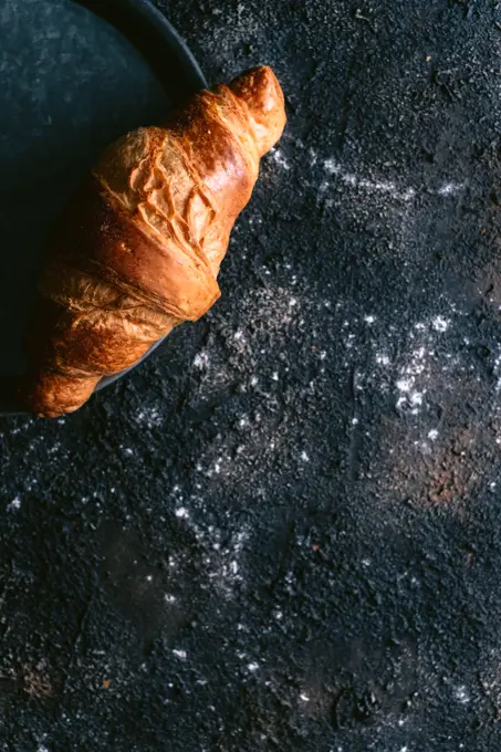 Top view of soft fresh bun placed on metal tray on messy black table during breakfast