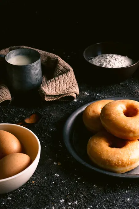 Fresh doughnuts placed on rough table near various pastry ingredients and utensils in kitchen