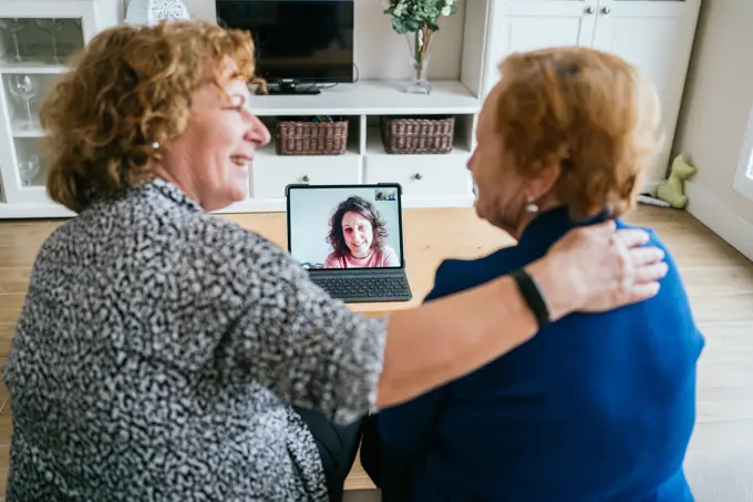 Back view of cheerful senior women chatting with friend during online video meeting via laptop while staying at home during coronavirus lockdown