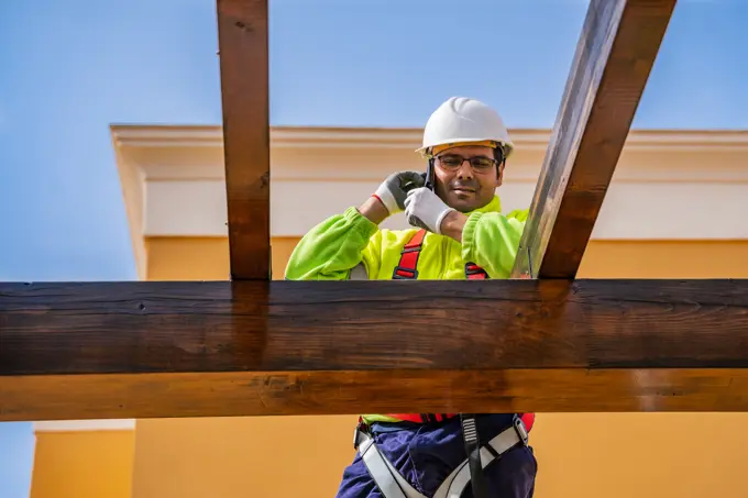 From below of male technician in work wear standing on scaffolding and preparing for installation of solar panel on wooden construction