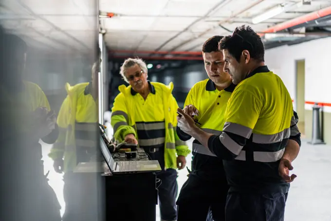 Group of skilled male engineers in uniform using gadgets while examining electrical equipment in modern building