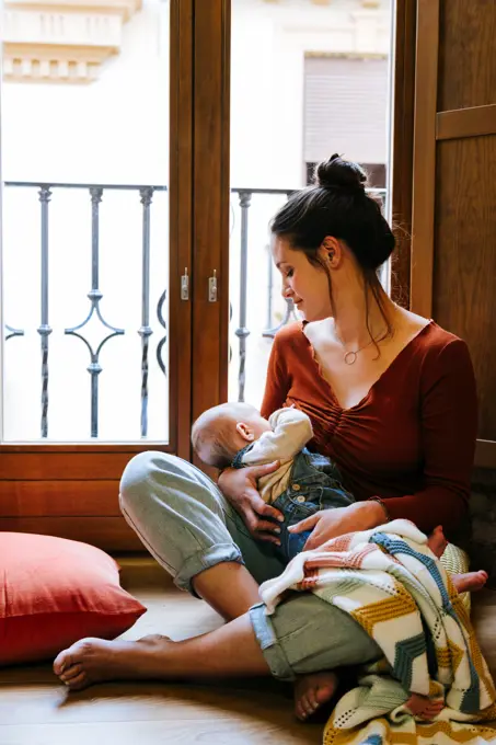 Happy mother breastfeeding baby near window