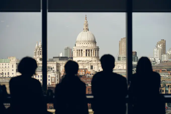 Back view silhouettes of travelers standing near window at viewpoint and admiring view of Saint Paul Cathedral in London