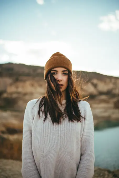 Youthful charming female tourist looking at camera while enjoying weekend journey to lake in autumn