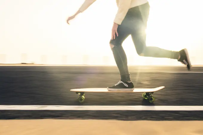 Unrecognizable guy in casual clothes riding skateboard on asphalt road in evening on Fuerteventura Island, Spain