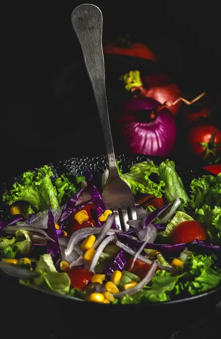 Healthy vegan food with fresh lettuce, cherries tomatoes, red onion and corn on dark background