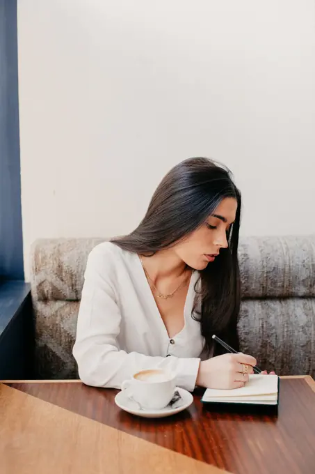 Brunette woman writing in a notebook in a bar