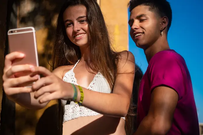 Charming young lady taking selfie on phone with content ethnic guy