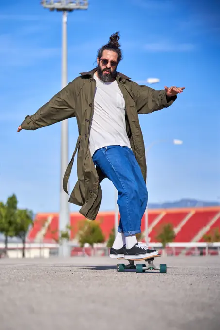 A Man skating on a skateboard on the road with his raincoat and sunglasses