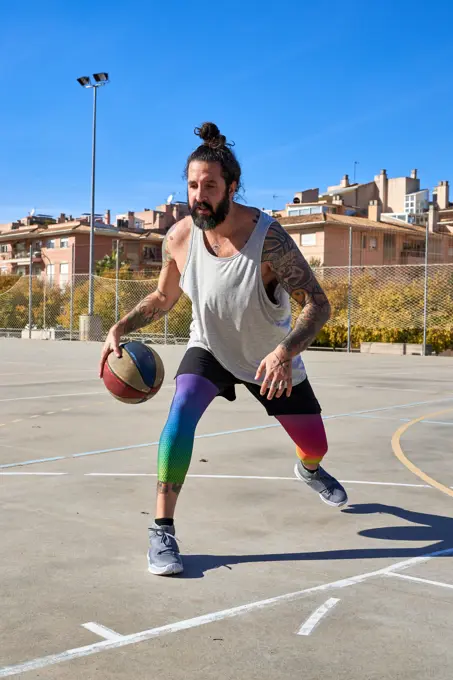 Man with a beard playing basketball on an urban court