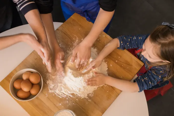 Children preparing dough while standing together at kitchen table with flour