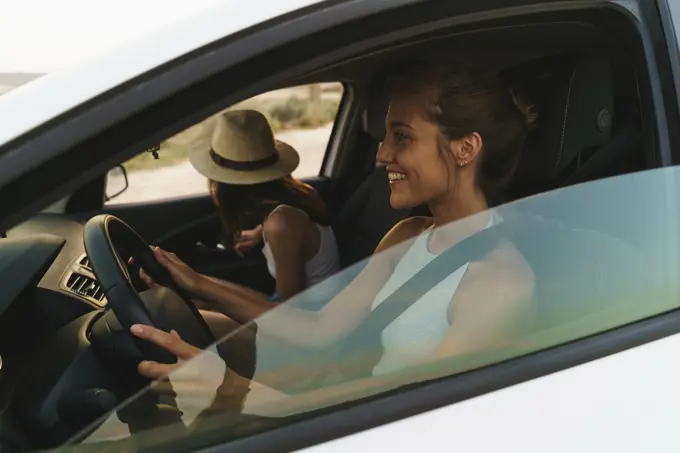 Side view of pretty young women riding a car in nature together.