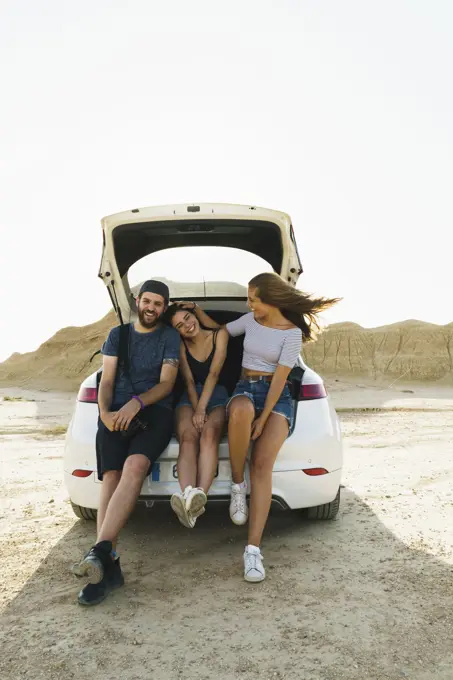 Cheerful man and women friends sitting in car trunk and having fun together.