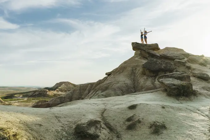 Unrecognizable women tourists standing on cliff and posing with hands up.