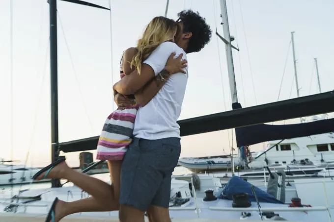 Side view of young loving couple embracing on pier with yachts on background.