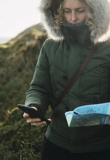 Pretty woman tourist with smartphone and map navigating in mountains.