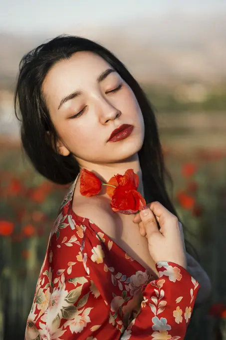 Gorgeous model in red dress holding poppy flowers