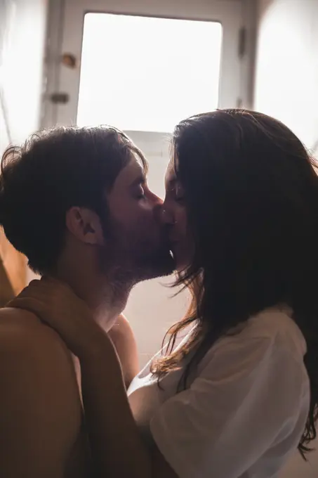 Young lovely pair sitting and kissing with eyes closed. Vertical indoors shot.