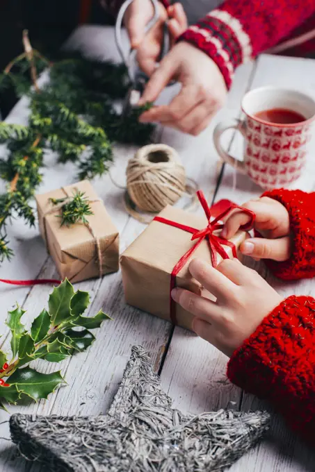 Kid and woman wrapping presents for Christmas on a wooden table with handcraft decoration 