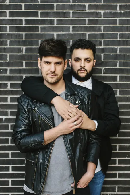 Gay couple hugging near brick wall