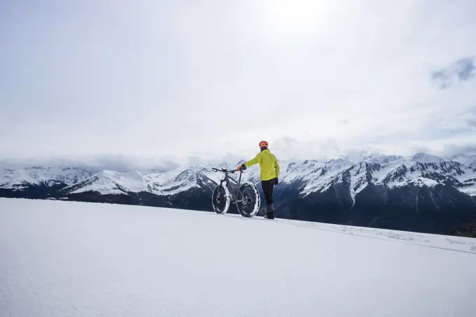 Unrecognizable tourist man walking on winter mountains with bicycle.