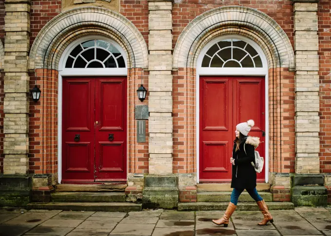 Side view of tourist woman walking at red doors of brick building on street in York, England