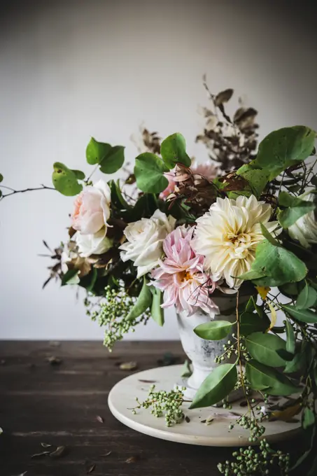 Concept of bouquet of dry and fresh roses, chrysanthemums and plant twigs in retro vase on wooden board on grey background