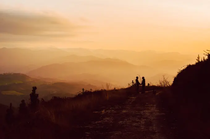 Side view of homosexual couple embracing near dog on route in darkness and picturesque view of valley in fog