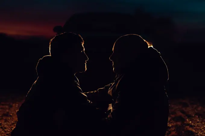 Side view of homosexual couple embracing and sitting on meadow in evening