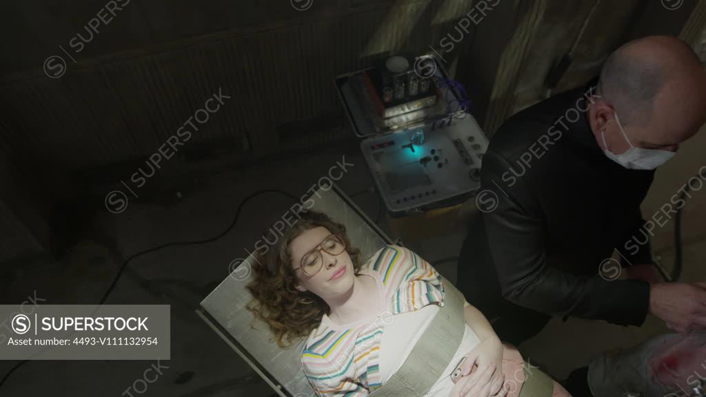 Evil dentist injecting mouth of shaking woman strapped to table / Cedar ...