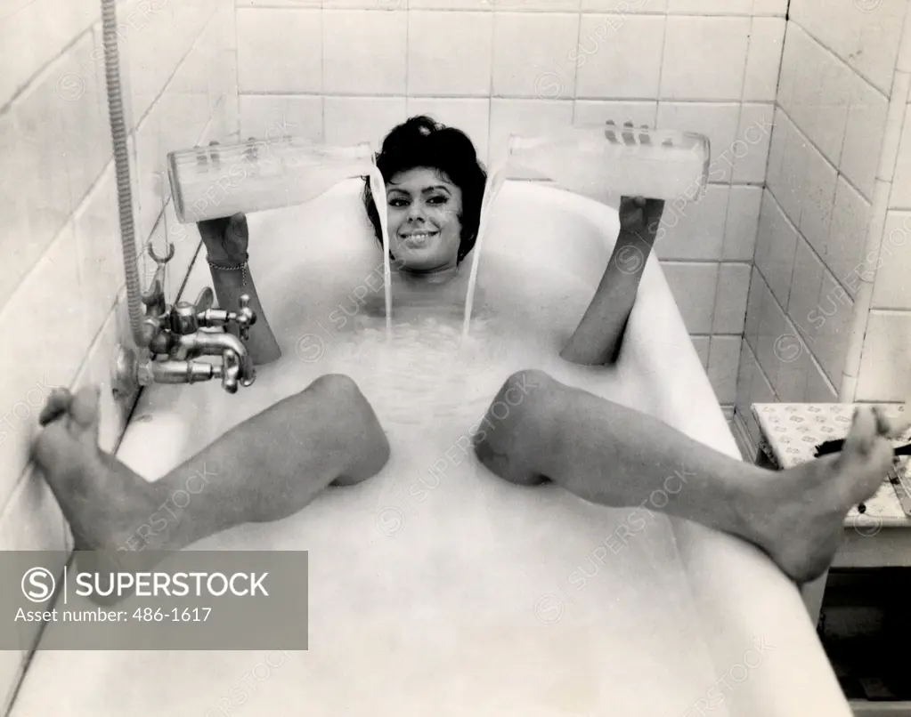 Portrait of woman in bubble bath pouring water from milk bottles