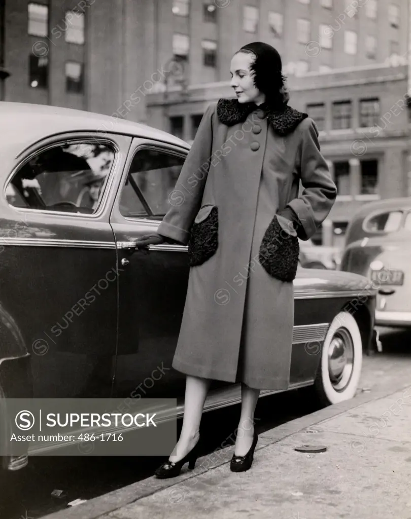 Mid adult woman wearing coat, posing in front of parked car, 1931