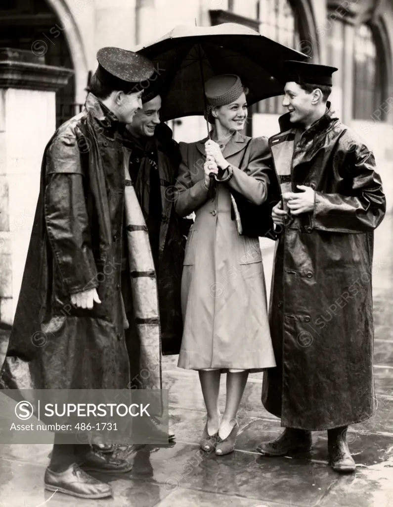 Woman with umbrella and three men in raincoats talking, 1931