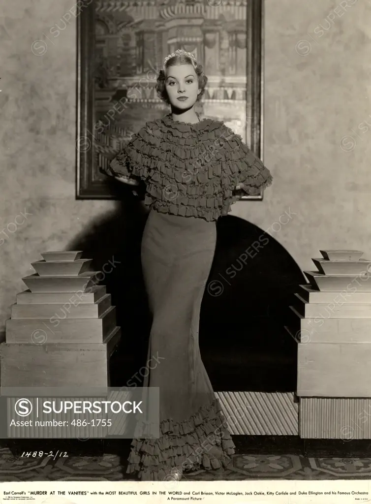 Portrait of young woman posing in long, frilly dress by armchair, 1931