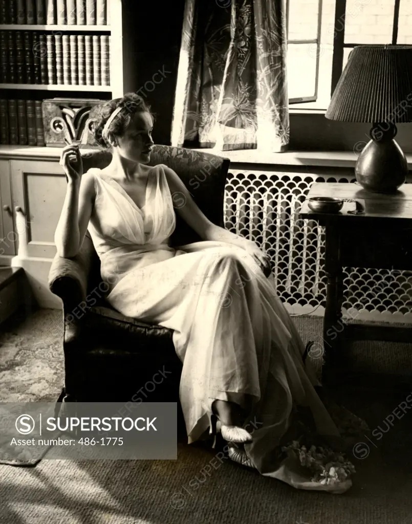 Young woman in white dress smoking cigarette while sitting in armchair