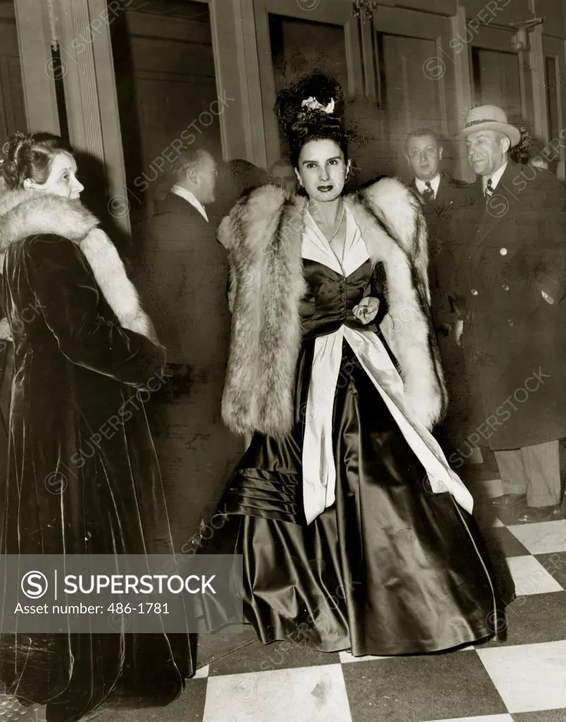 Young woman wearing ball gown and fur coat, people in background