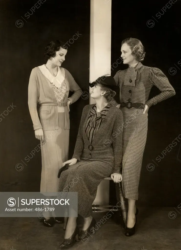 Three women posing in studio, one sitting