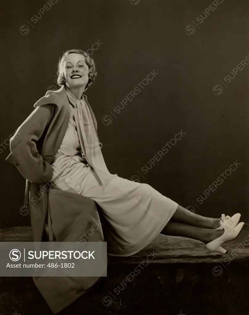 Young woman sitting cross-legged in coat, smiling