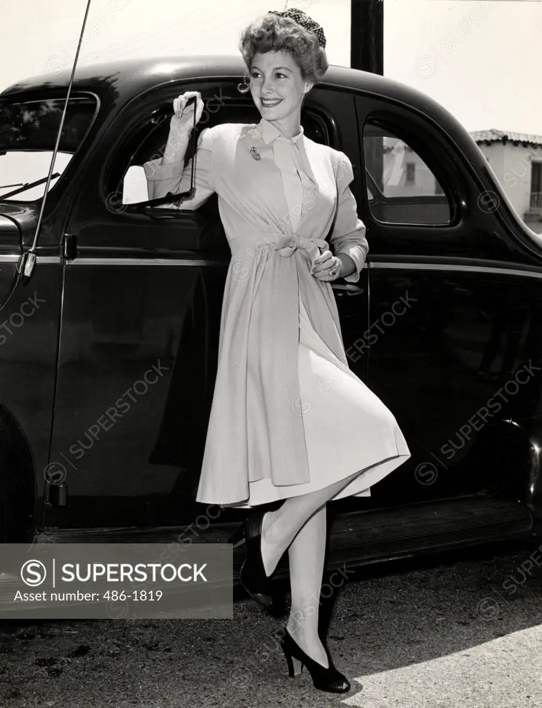 Mid adult woman posing in elegant clothing in front of car