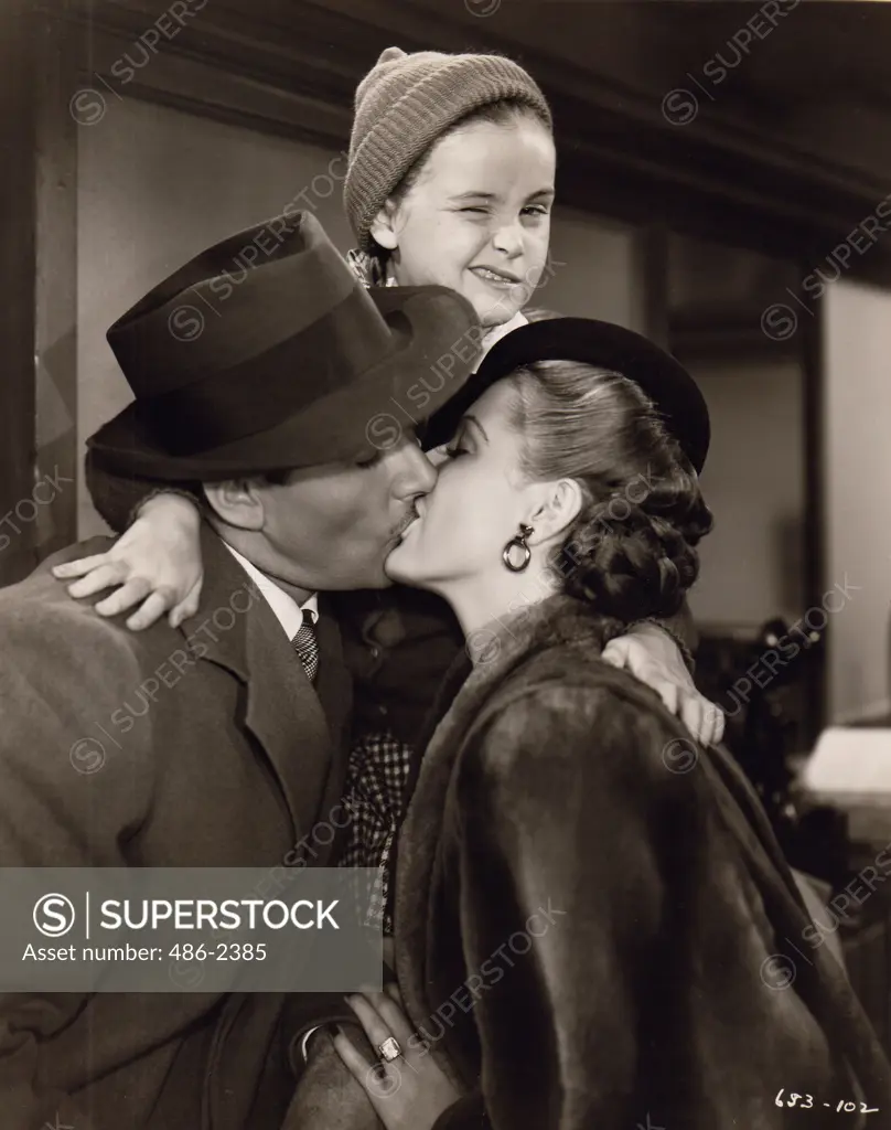 Couple kissing while boy is embracing them and winking towards camera