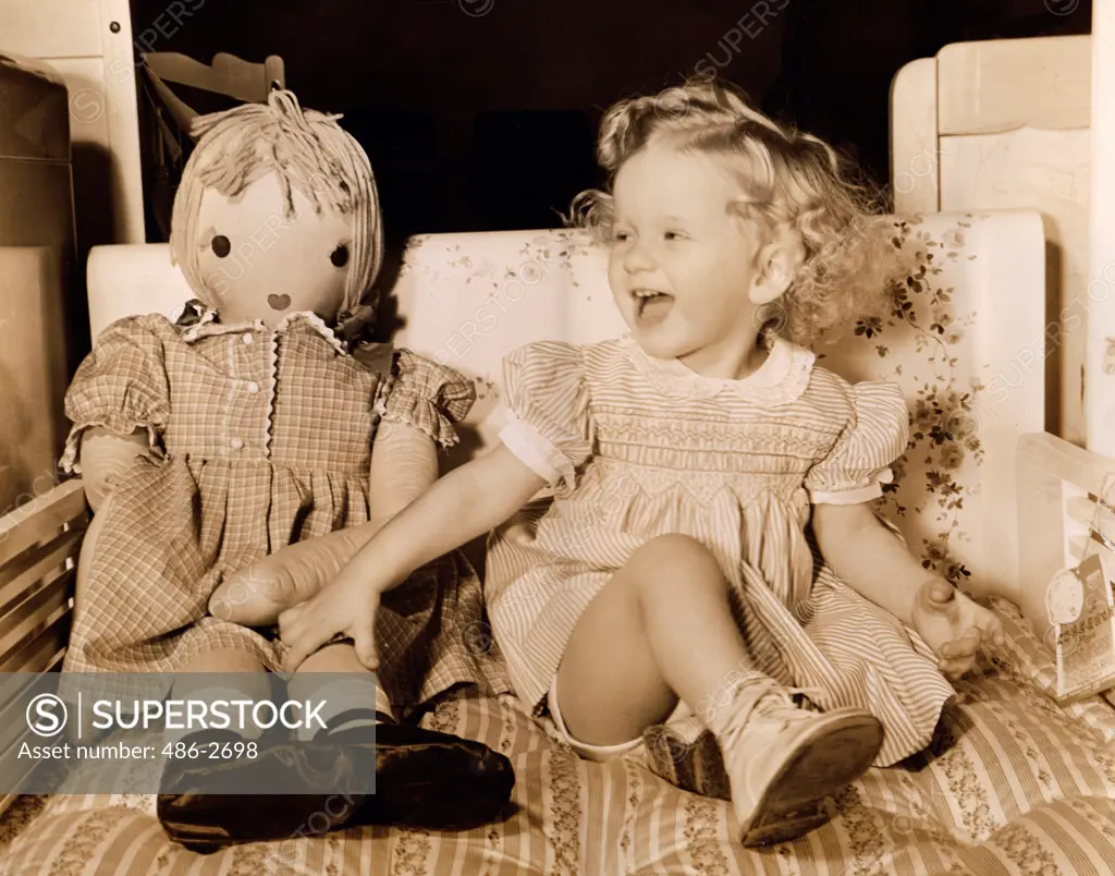 Girl sitting with her doll and laughing