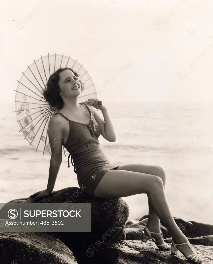 Attractive woman wearing swimming suit sitting on boulder on beach