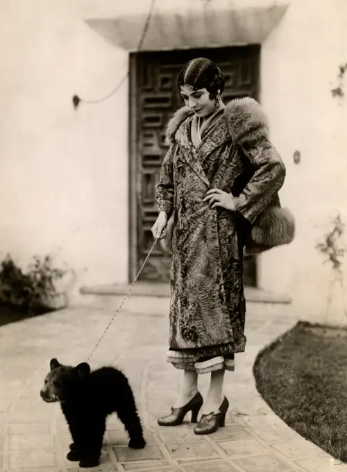 Elegant woman holding bear cub on leash