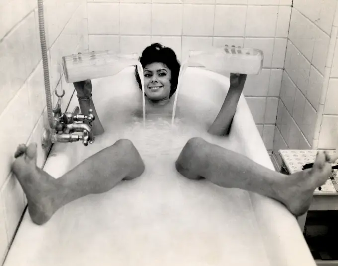 Portrait of woman in bubble bath pouring water from milk bottles